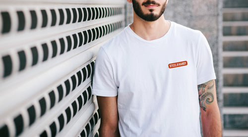 Existing Steel & Hardy design reference: white T-shirt with the original orange wordmark at the chest. Concept, not a finished item for sale.